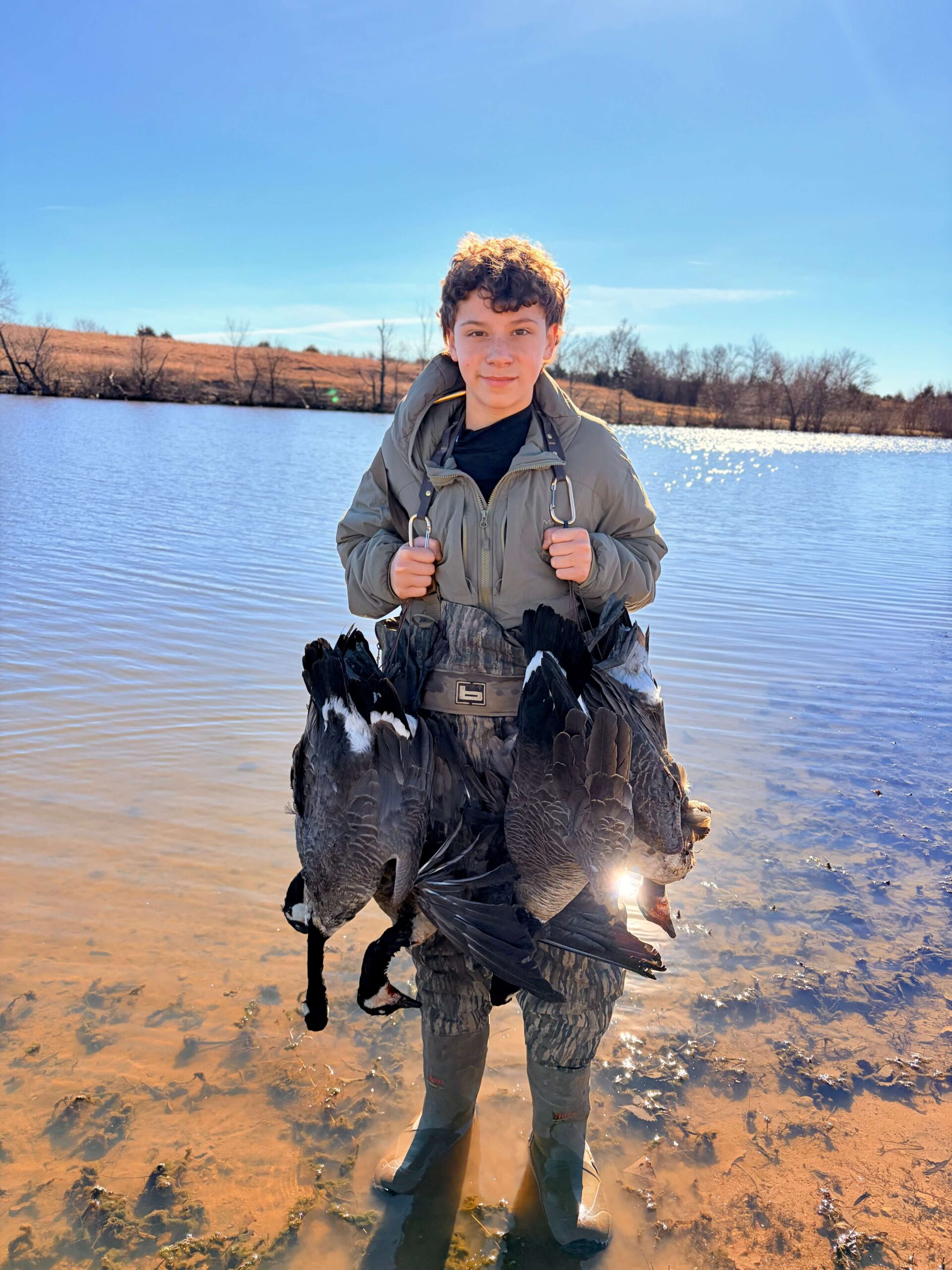 young hunter holding geese while standing in water