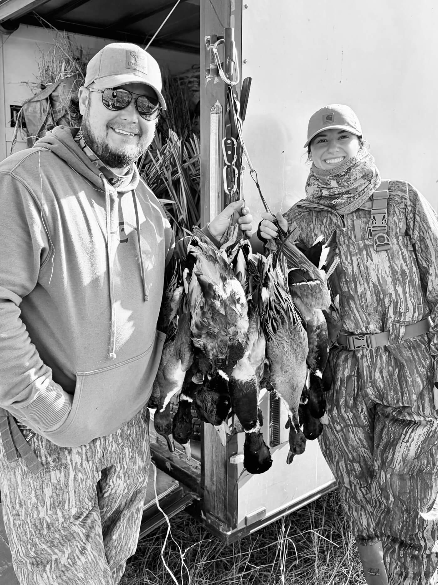 two hunters holding ducks by a trailer, black and white